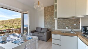 A modern kitchen with a stone backsplash, a grey sofa, and a dining area with a table and chairs.