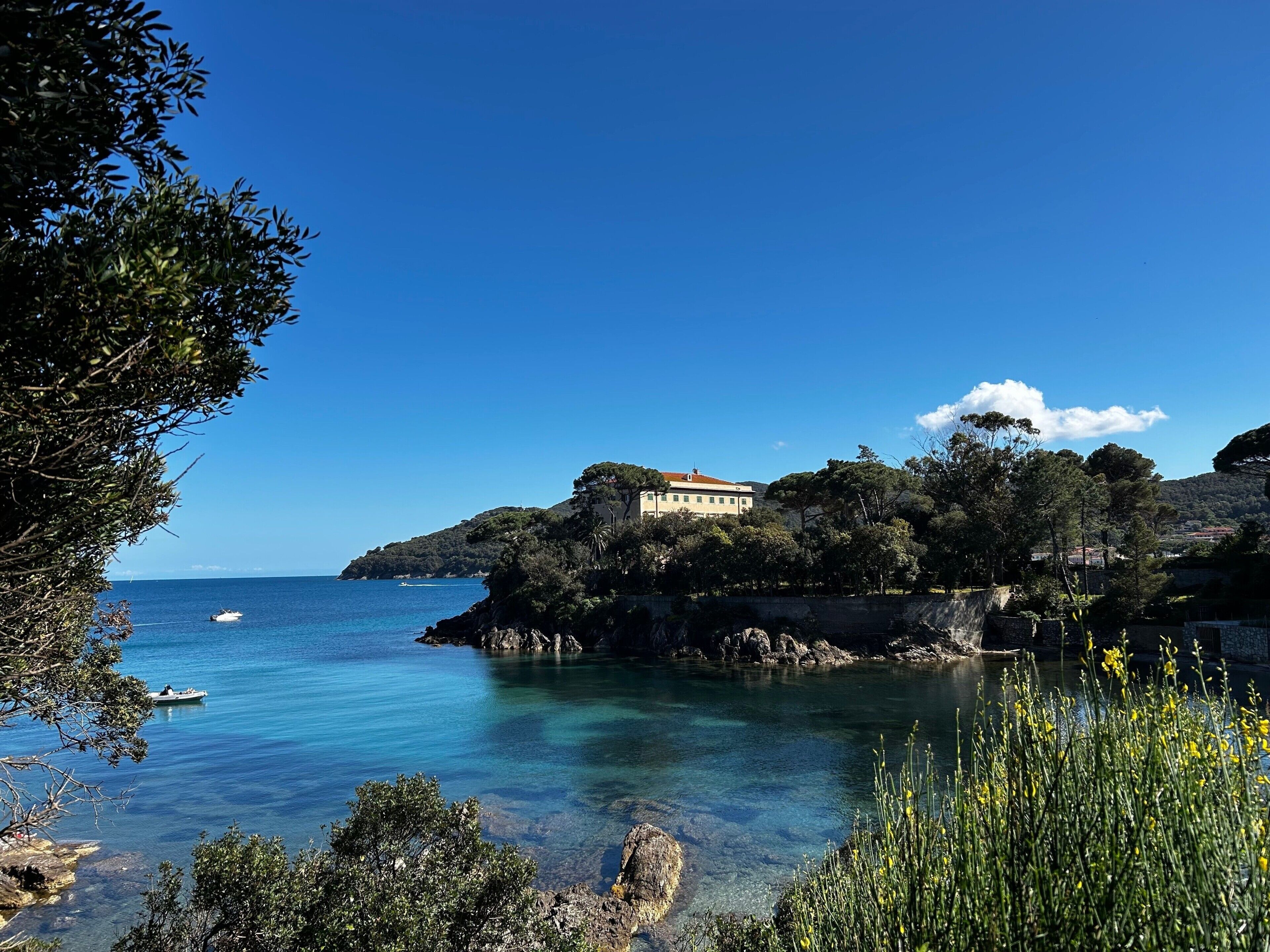 A coastal view with a building on a cliff, clear blue sea, and rocky shoreline.