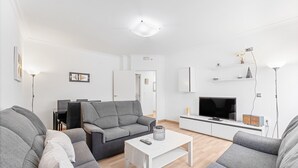 A modern living room with a grey sofa set, a white coffee table, a flat-screen TV, and a minimalist decor.