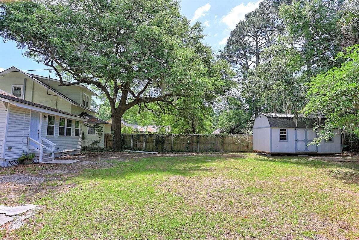 Spacious, peaceful backyard with plenty of open lawn, mature shade trees, and a charming cottage-style outbuilding tucked among the greenery.