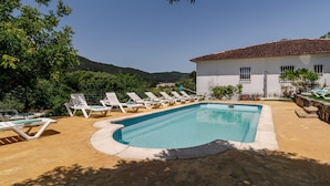 Una piscina con sillas de descanso, un edificio de techo azulejado y montañas al fondo.