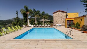 Una piscina con sillones de descanso, un edificio de piedra y vistas a las colinas.