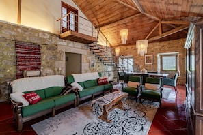 Un intérieur rustique avec un mur en pierre, un escalier en bois, des canapés verts et un coin repas.