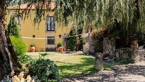 Un patio con un edificio amarillo, plantas en macetas, un muro de piedra y un sendero adoquinado.