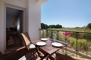 Un balcone con un tavolo apparecchiato per due, una sedia e vista su spazi verdi e edifici in lontananza.