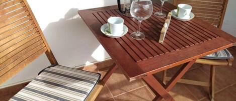 Una mesa de madera con sillas, una cafetera, copas de vino y tazas.