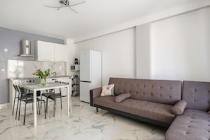 A modern kitchen with a dining table, chairs, a sofa, and a refrigerator.