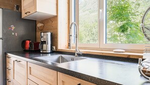 Eine Küche mit Holzausstattung, einer Edelstahl-Spüle, einer Kaffeemaschine und einem Fenster mit Blick ins Grüne.