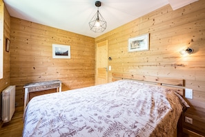 A wooden-paneled room with a bed, a table, and a radiator.