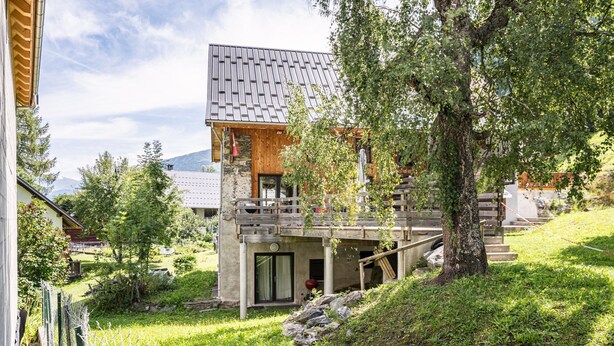 Ein modernes Haus mit geneigtem Dach, einer Holzterrasse und einem Steinfundament.