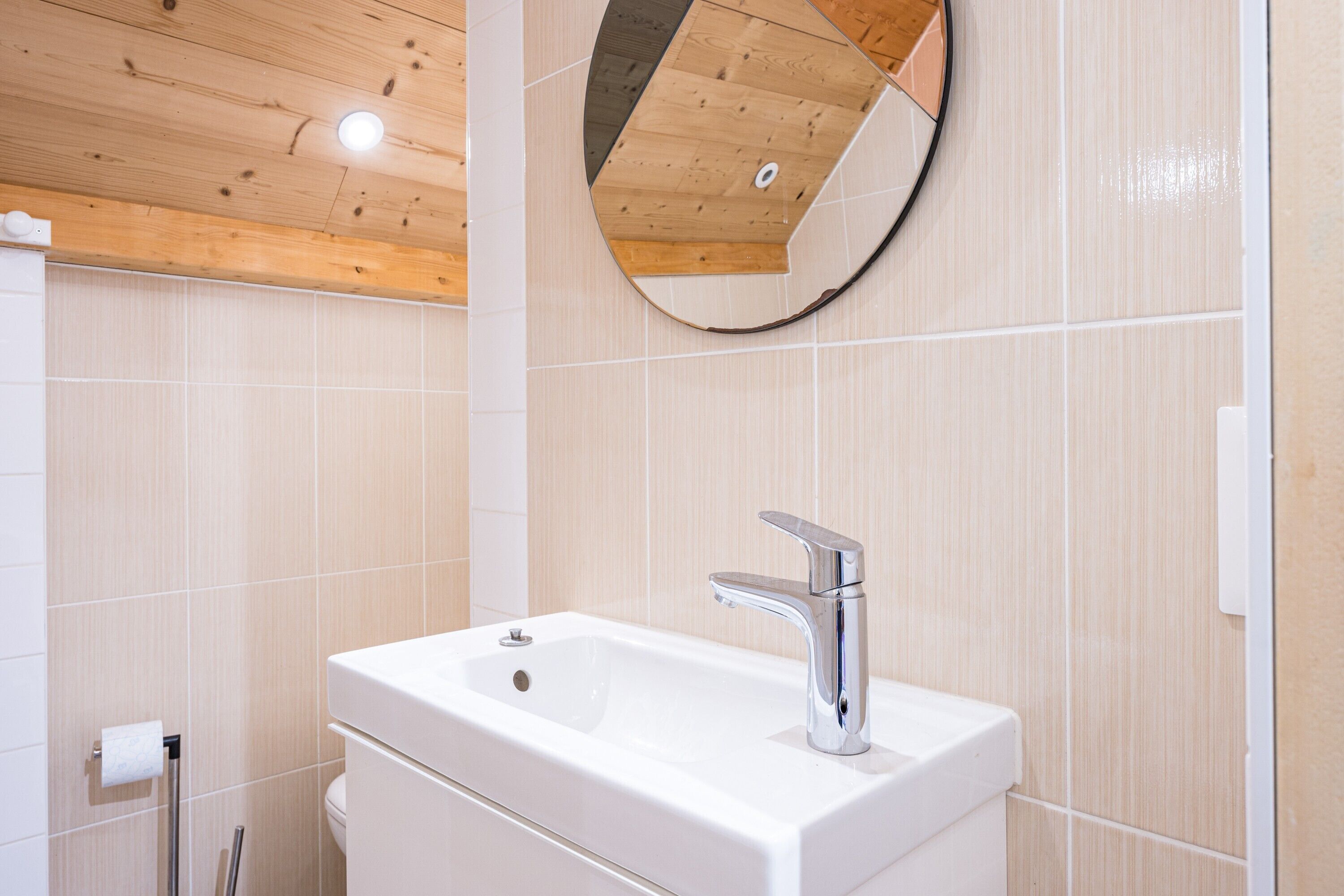 A bathroom with a white sink, a mirror, and wooden ceiling.