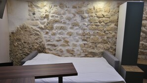 Una stanza con una parete in pietra, un letto e un tavolo.