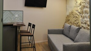 Un ambiente compatto con divano, tavolo da pranzo con sedie, TV a schermo piatto montata a parete e una parete decorativa in pietra.
