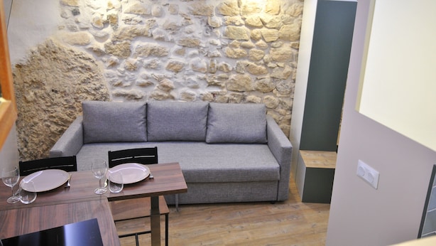 Una stanza con parete in pietra, divano grigio, tavolo di legno con sedie e un set da pranzo.