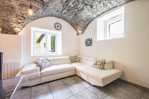 A modern living room with a stone ceiling, a white sectional sofa, a clock, and a window with a view.