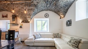 Una sala de estar moderna con techo de piedra, un sofá blanco, una mesa de comedor y una cocina al fondo.