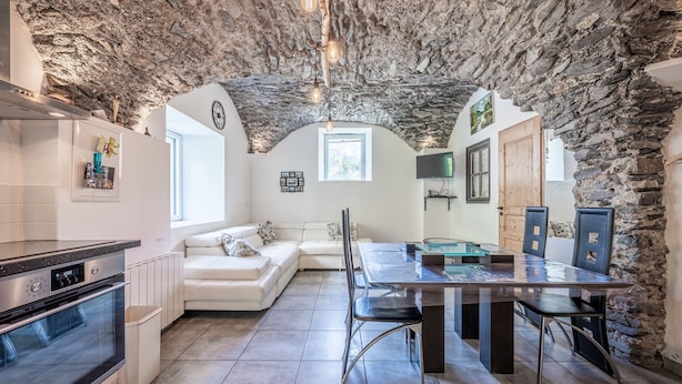 Una cocina con techo de piedra, un comedor con mesa de vidrio y un sofá blanco.