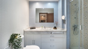 Een badkamer met een wit toilet, een wastafel met spiegel erboven, een douchegedeelte en een pot met een plant.