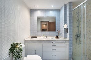 Een badkamer met een wit toilet, een wastafel met spiegel erboven, een douchegedeelte en een pot met een plant.