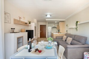 Un espai de vida modern amb zona de menjador, cuina i un sofà gris.