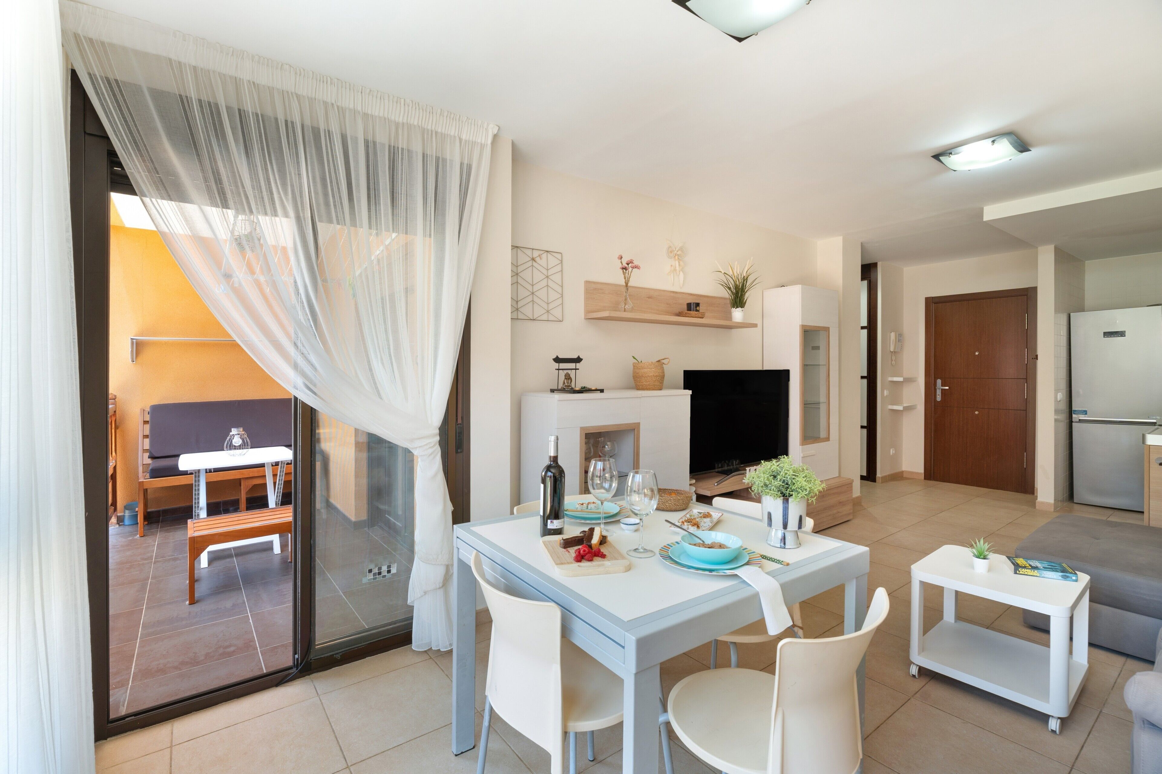 Una cocina moderna con refrigerador incorporado, un comedor con mesa y sillas, y una sala de estar con sofá y televisor.