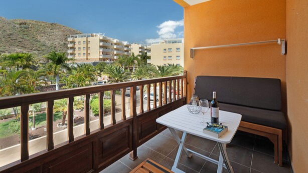 Een balkon met een tafel, een bank en uitzicht op gebouwen en palmbomen.