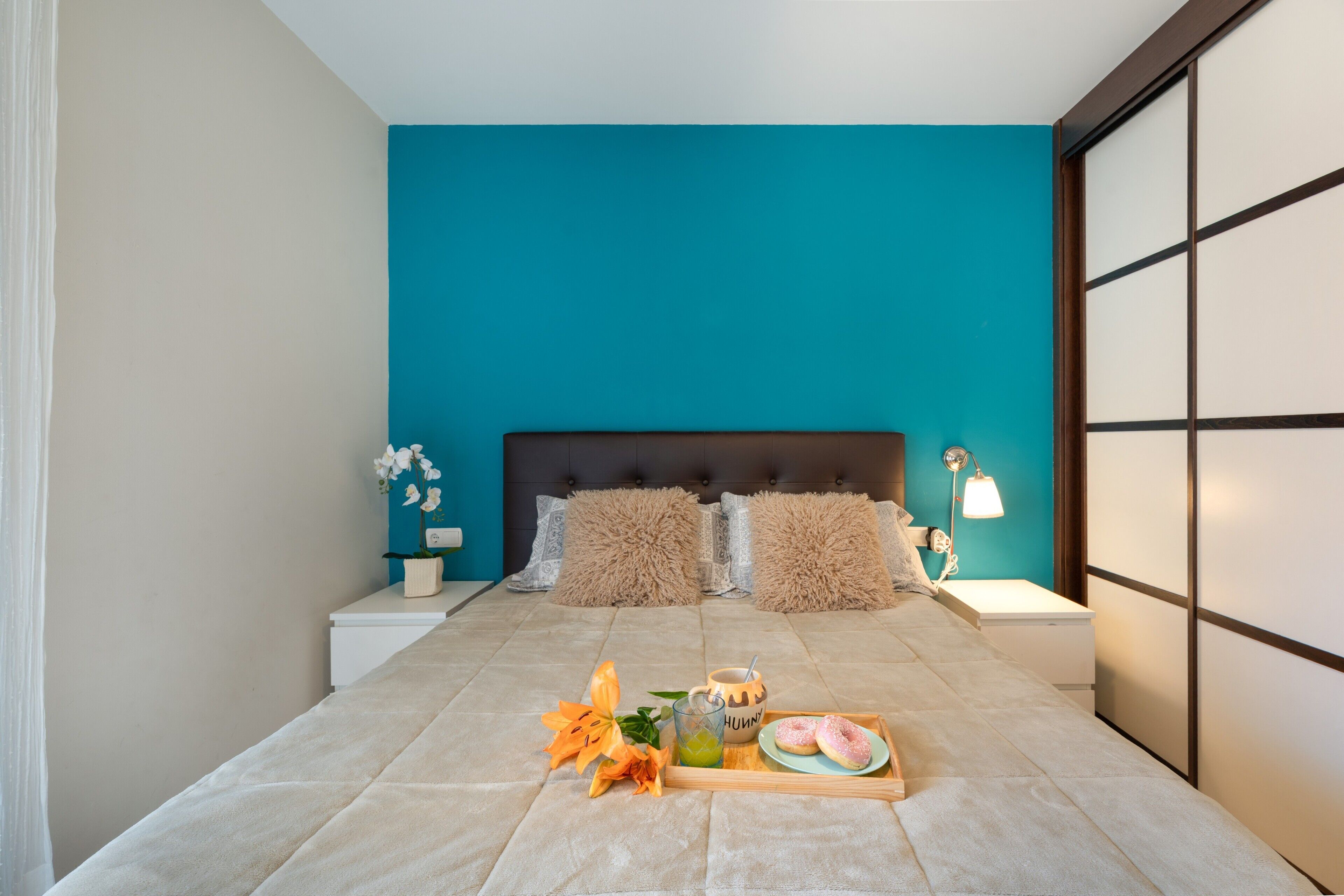 Un dormitorio moderno con una pared de acento color verde azulado, un cabecero capitonado y una mesita de noche con una lámpara.