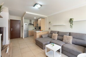 A modern living room with a grey sofa, a white coffee table, and a kitchen in the background.
