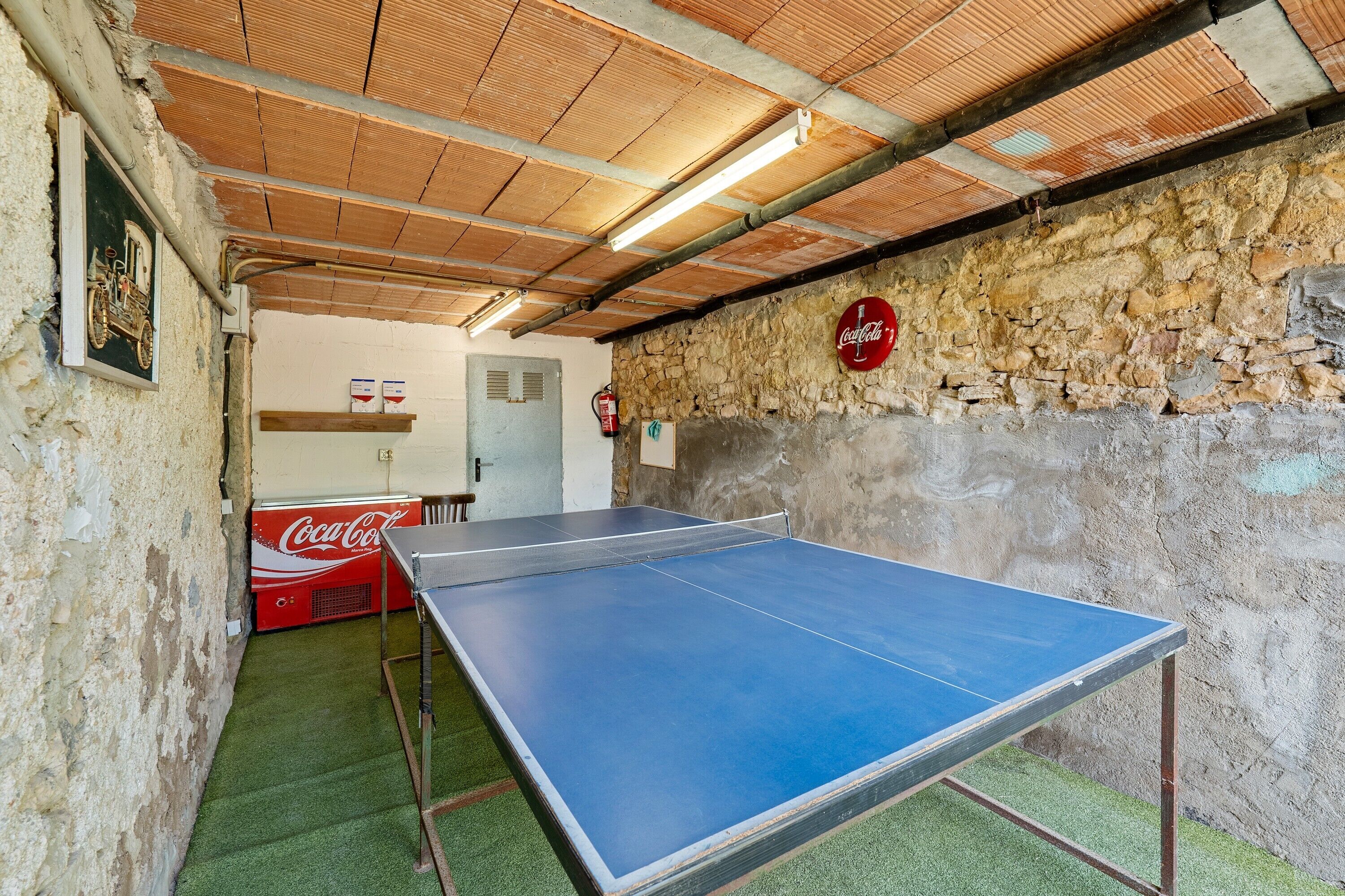 Una mesa de ping pong en una habitación con paredes de piedra, un refrigerador de Coca-Cola y un extintor.