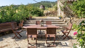 A patio with a round table and chairs, surrounded by stone walls and greenery. - Country House 'Caltiku' with Mountain View, Private Pool and Private Terrace (els Ranxos de Bonany)
