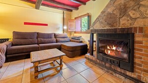 A cozy living room with a stone fireplace, a sectional sofa, and a wooden coffee table. - Country House 'Caltiku' with Mountain View, Private Pool and Private Terrace (els Ranxos de Bonany)