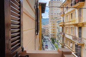 Une vue étroite d’une rue depuis un balcon, avec des bâtiments de chaque côté et une montagne en arrière-plan.
