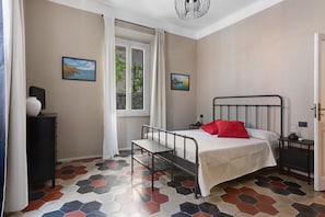 Une chambre à coucher comprenant un lit, une table de chevet, une commode, une fenêtre avec des rideaux et un revêtement de sol à motifs hexagonaux.