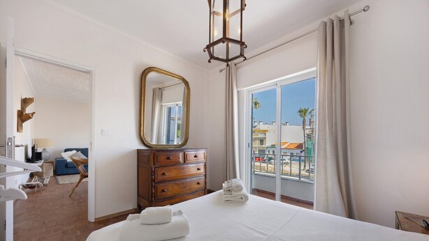 A hotel room with a bed, a dresser, a mirror, and a view of the outside. - Apartment 'Regato' with Private Terrace, Balcony and Wi-Fi (Ferragudo)