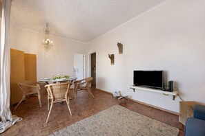 A living room with a dining table, wicker chairs, a chandelier, a flat-screen TV, and a wooden coffee table.