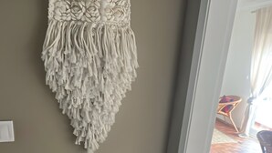 A macramé wall hanging with a fringe bottom, hanging on a white wall. - Apartment 'Regato' with Private Terrace, Balcony and Wi-Fi (Ferragudo)