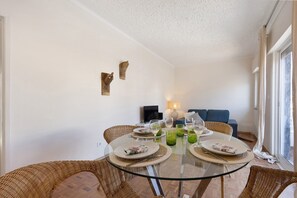 Un comedor con una mesa de vidrio, sillas de mimbre y un sofá al fondo.