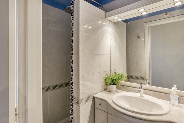 A bathroom with a shower, a sink with a mirror, and a potted plant.