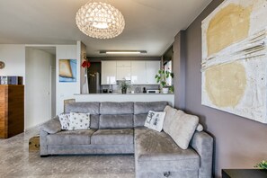 A modern living room with a grey sectional sofa, a decorative light fixture, and a large abstract painting on the wall.