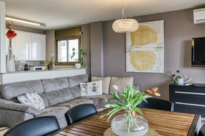 A modern living room with a grey sofa, a wooden dining table, and a clear glass vase with flowers.