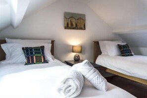 Une chambre d’hôtel avec deux lits, un tableau au mur, une lampe sur une table de chevet et une serviette roulée sur le lit.