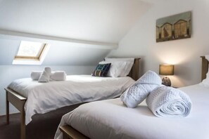 Une chambre d’hôtel avec deux lits, une lucarne, un tableau au mur et une lampe de chevet.