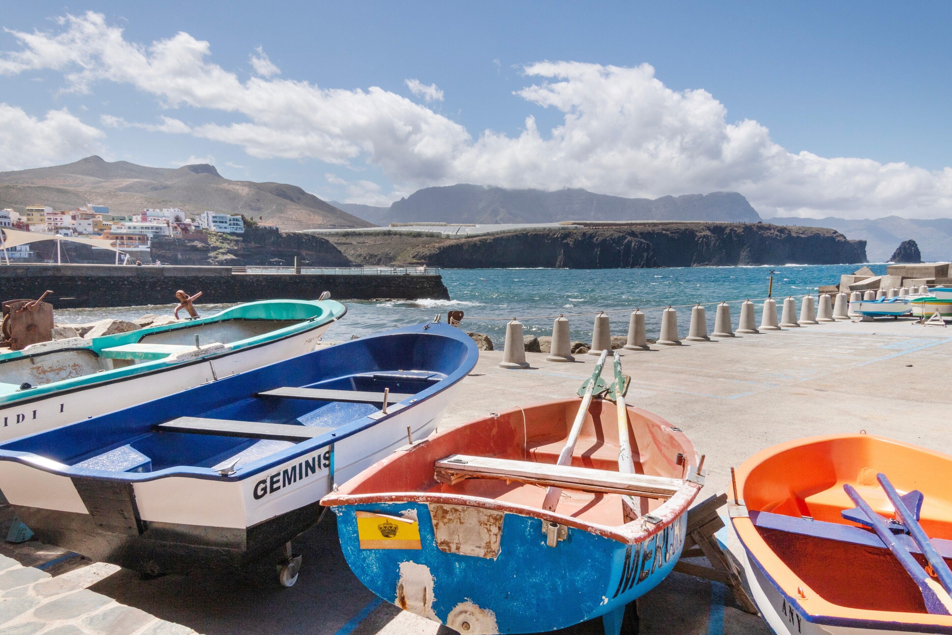Un port où sont amarrés des bateaux, une jetée et, en arrière-plan, un paysage montagneux.