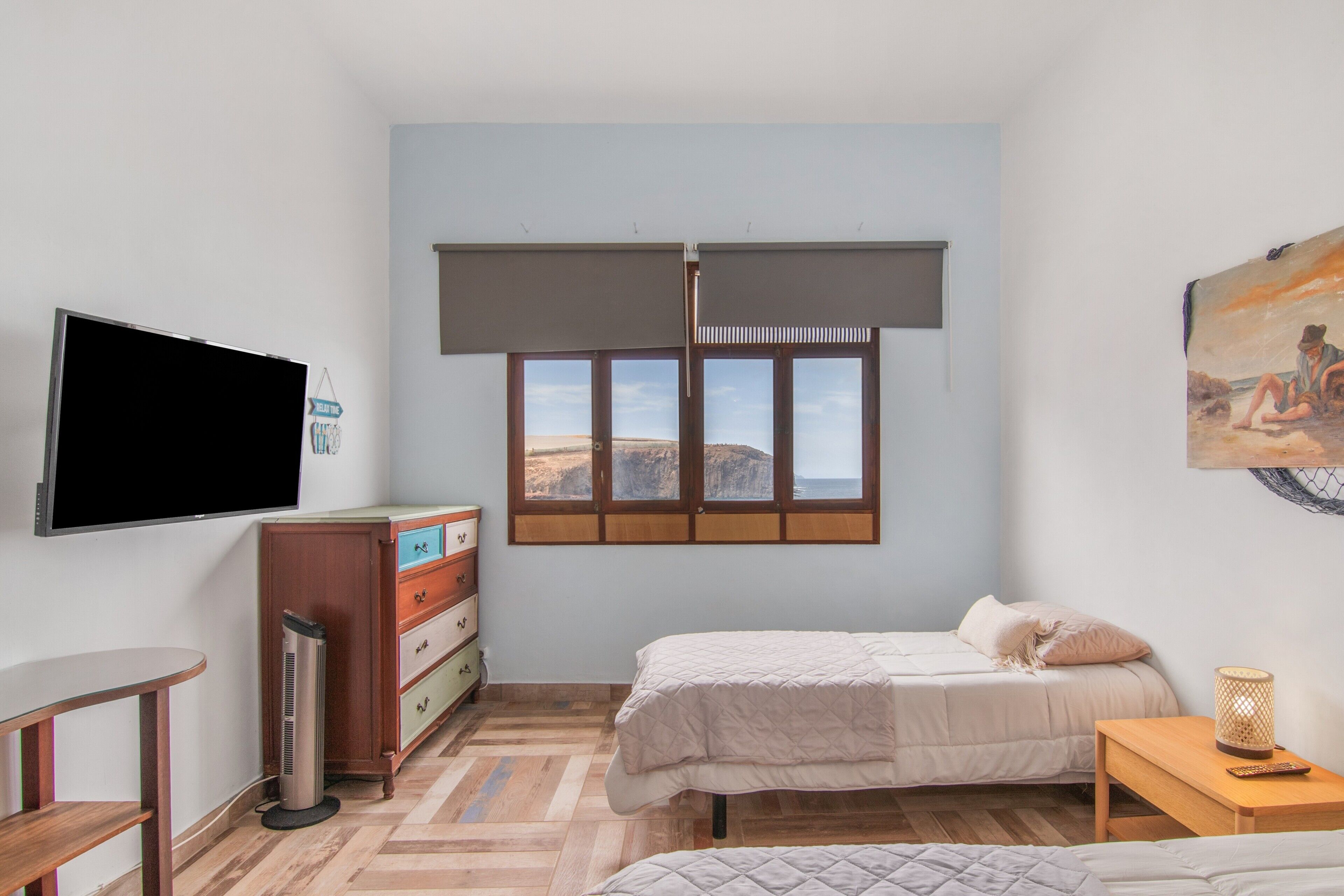 Un dormitorio con cama, escritorio, televisor, cómoda y ventana con vistas.