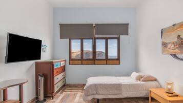 Un dormitorio con cama, escritorio, televisor, cómoda y ventana con vistas.