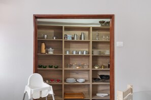 A kitchen with wooden shelves, a white chair, and various kitchenware. - Vacation 'Las Velas' with Sea View, Wi-Fi and Air Conditioning (Gáldar)
