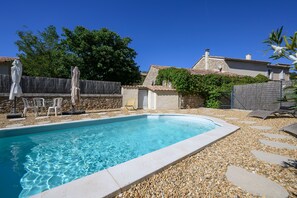 A swimming pool with clear water, surrounded by pebbles and steps leading to a covered seating area.