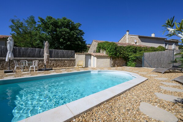 Una piscina rectangular con agua cristalina, rodeada de guijarros y un muro de piedra.