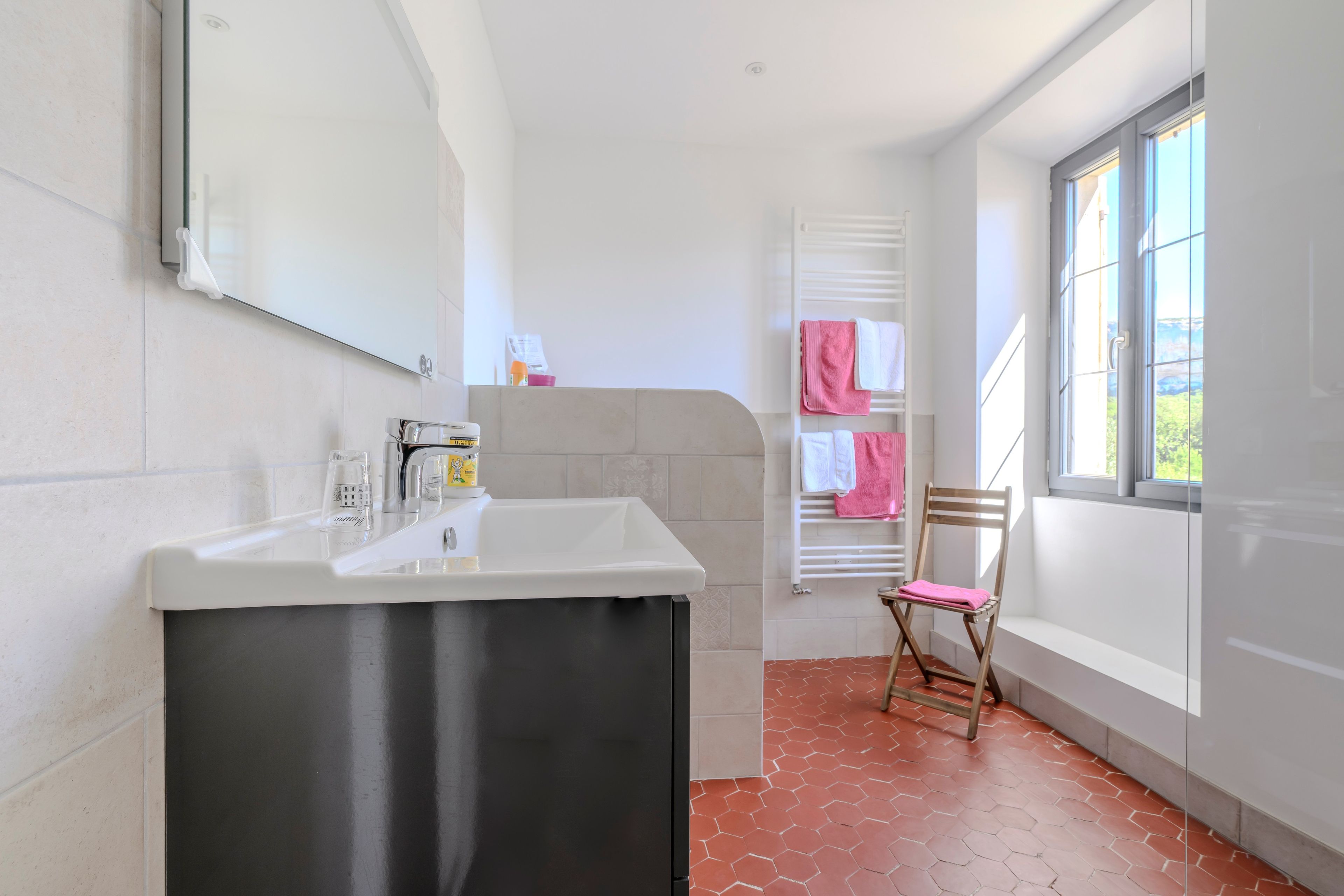 Ein Badezimmer mit einem weißen Waschbecken, einem Spiegel, einem Handtuchhalter mit rosafarbenen Handtüchern und einem Fenster mit Blick.