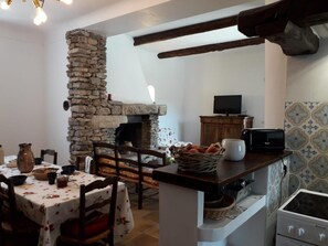 Cozinha acolhedora com lareira de pedra, mesa de jantar com toalhas florais e micro-ondas na bancada.